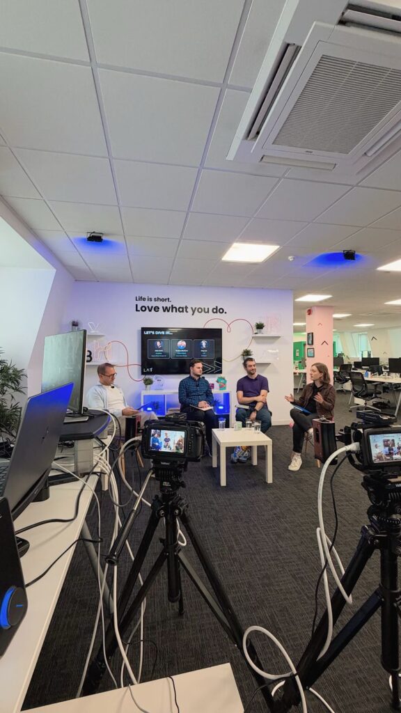 Four people seated in discussion in the distance, with two cameras on tripods in the foreground