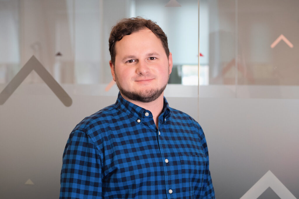 Yordan Dimitrov with a closed-mouth smile, wearing a blue checked shirt against a frosted-glass background