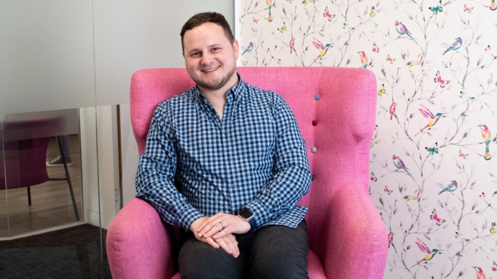 Yordan Dimitrov smiling, seated in a pink armchair in front of floral wallpaper