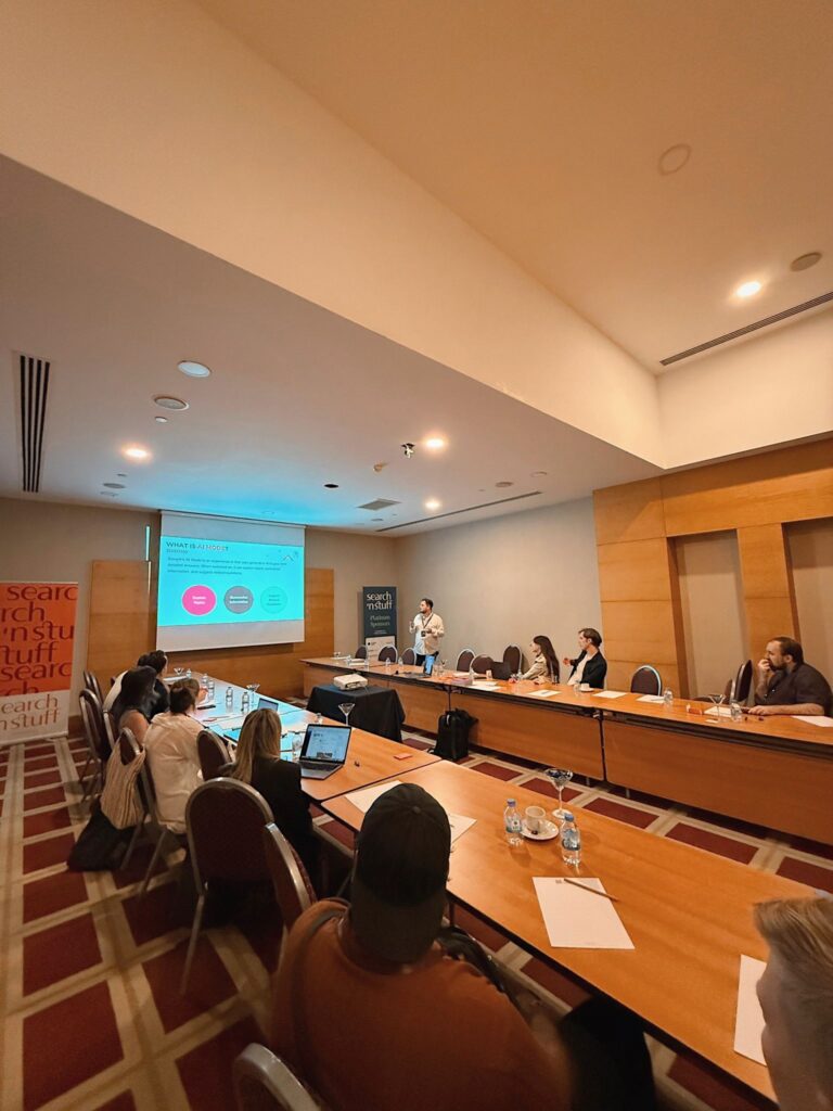 Attendees seated along long tables in a wood-panelled room, facing a presentation screen at the far end