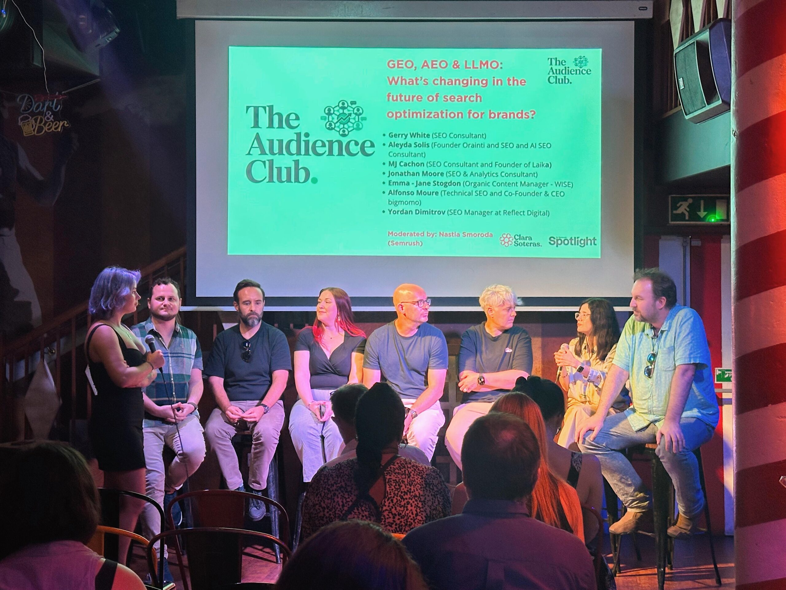 Panel of speakers seated on stage beneath a screen showing a The Audience Club slide