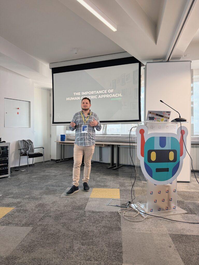 Yordan Dimitrov presenting in a conference room, with a projector screen behind him and a robot figure beside him