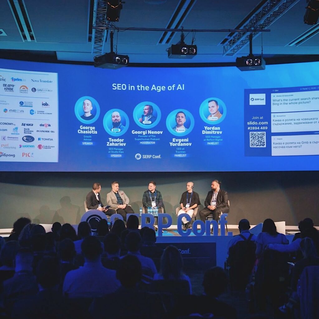 Yordan Dimitrov seated with four other panellists on a stage, with the audience in the foreground